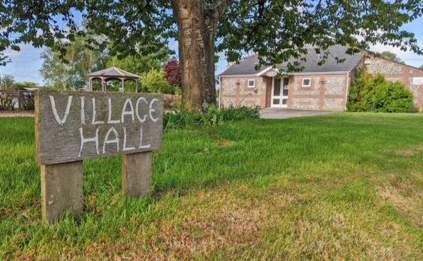 Wooden village hall sign and village hall in the background