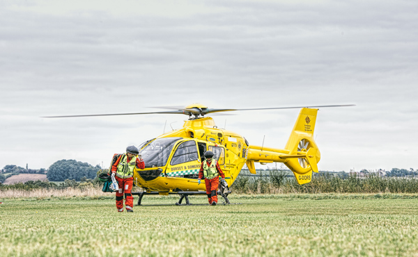 Two air ambulance crew members in front of the yellow helicopter that signifies Dorset and Somerset Air Ambulance
