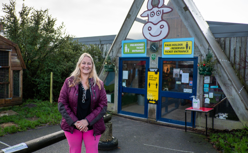 A lady stands smiling in front of Farmer Palmers entrance, in Poole, Dorset. 