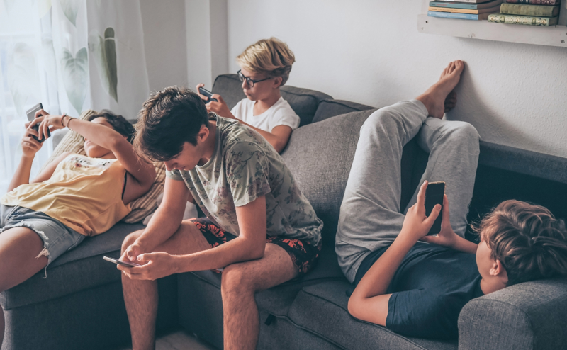 Several boys sat on a sofa with mobile phones